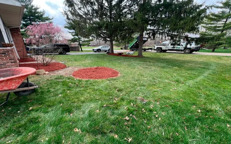 A suburban yard undergoing landscaping improvements with red mulch, a wheelbarrow, and parked service vehicles, captured as part of a Spring CleanUp in Ohio.