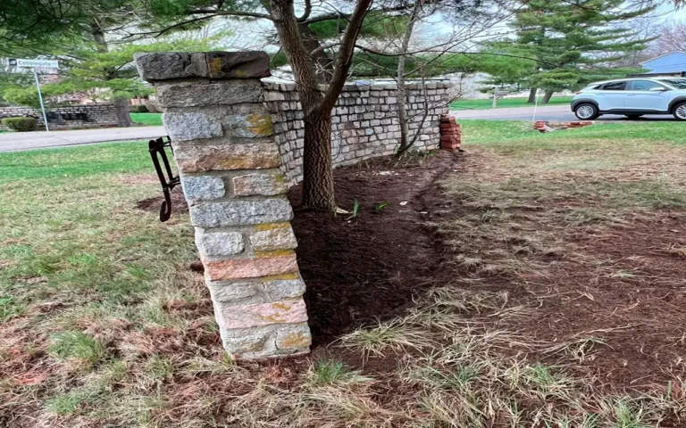 A well-maintained stone wall with a pillar, surrounded by a cleaned landscape in preparation for a Spring CleanUp in Ohio. A tree stands nearby, with cleared soil around its base, enhancing the yard’s appearance.
